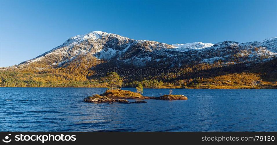 Norwegian autumn landscape a?? fjord and distant snow-capped mountains, blue clear water and rocky island with pines