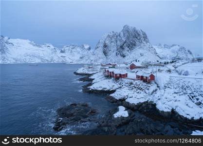 Norwegian fishing village at twilight in Hamnoy City, Lofoten islands, Norway, Europe. White snowy mountain hills and trees at night, nature landscape background in winter season.