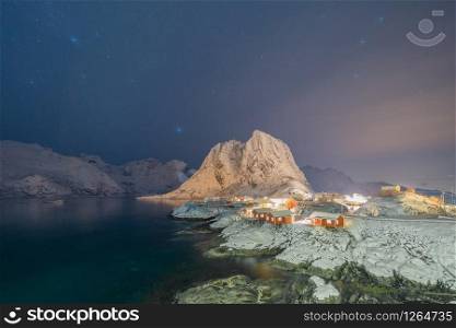 Norwegian fishing village with stars in Hamnoy City, Lofoten islands, Norway, Europe. White snowy mountain hills and trees at night, nature landscape background in winter season.