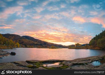 Norwegian fjord landscape with sunset at autumn time. Colorful sky, pastel water and motley mountains.