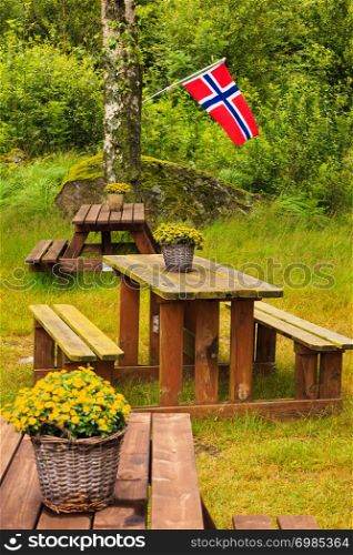 Norwegian flag and picnic site wooden table and benches outdoor in green forest park, Europe.. norwegian flag and green picnic site