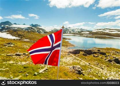 Norwegian flag waving against snowy mountains landscape, summertime. National tourist route Sognefjellet.. Norwegian flag and mountains snowy landscape