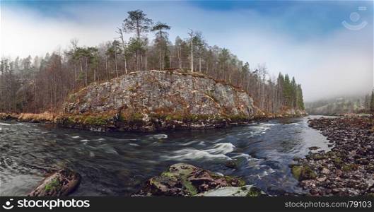 Norwegian landscape with mountain river flow. Autumn forest and mossy rocks around.