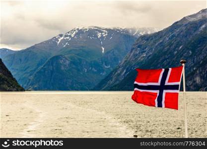 Norwegian national flag waving in the wind in Sogne fjord with mountains in the background, Aurlan, Sogn og Fjordane county, Norway