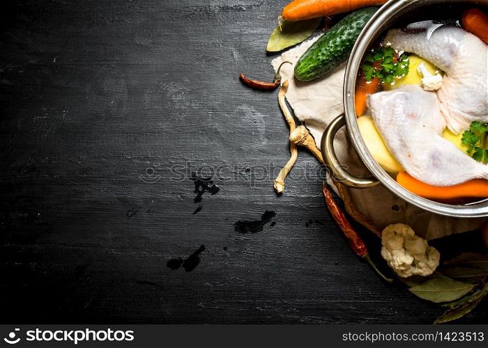 Not boiled chicken soup with fresh vegetables and spices. On a black wooden background.. Not boiled chicken soup with fresh vegetables and spices.