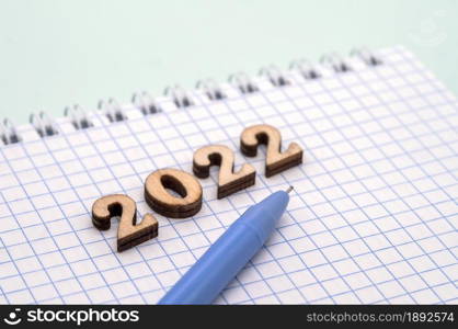 Notebook and pen on the blue. Wooden numbers date 2022. A blank sheet of paper and a blue pen.. Notebook and pen on the table. Wooden numbers date 2022. A blank sheet of paper and a ballpoint pen.