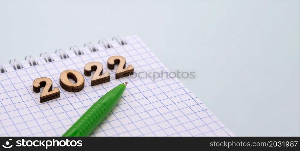 Notebook and pen on the blue. Wooden numbers date 2022. A blank sheet of paper and a green pen.. Notebook and pen on the table. Wooden numbers date 2022. A blank sheet of paper and a ballpoint pen.