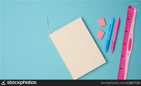 notebook and pink ruler on blue background, top view