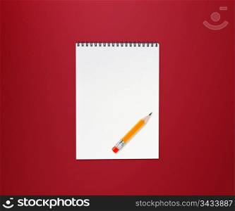 Notebook and small yellow pencil with eraser on red background