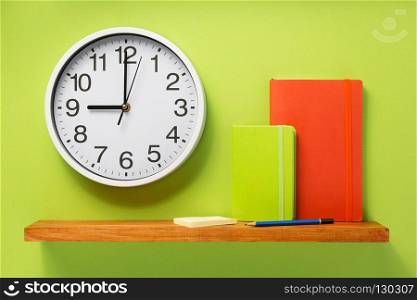 notebook and wall clock on shelf at wall background surface