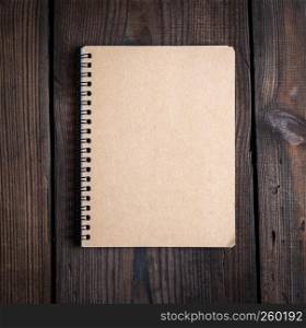 notebook on a black iron spring with brown empty sheets on a brown wooden background, close up