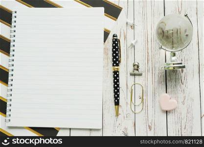 Notebook on a spring, pen, carnations, paper clips and a glass globe on a striped paper and gray wooden background. Work at home. Copy space.