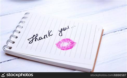 notebook paper with a line with an inscription thank you and kiss imprint of lipstick red lipstick