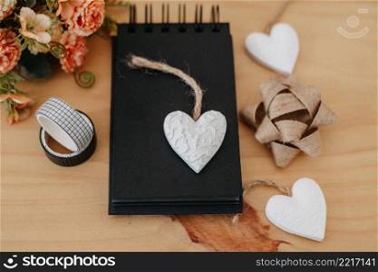 notebook with black sheets with copy space, on a wooden table with a bouquet of flowers and a white heart.