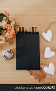 notebook with black sheets with copy space, on a wooden table with a bouquet of flowers and a white heart.