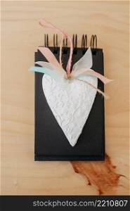 notebook with black sheets with copy space, on a wooden table with a white heart.