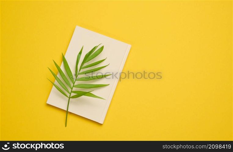 notebook with blank white sheets on a yellow background, top view.