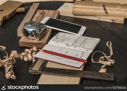 notebook with drawings, chips, pencil, tape measure, smartphone, square and plane on a black table