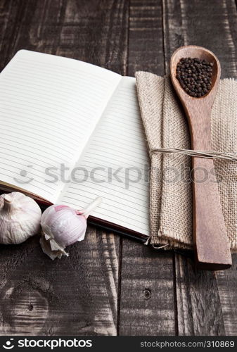 Notebook with pepper on spoon and kitchen towel on wooden board