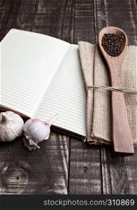 Notebook with pepper on spoon and kitchen towel on wooden board
