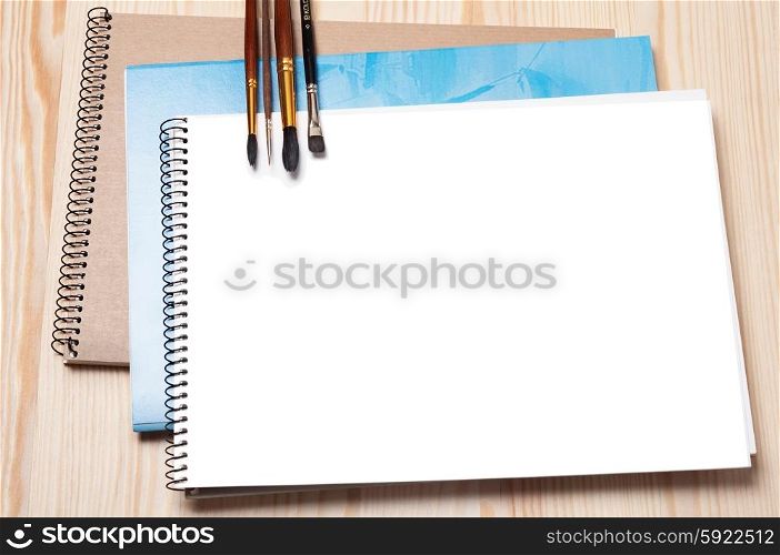 Notebooks and brushes on a wooden background