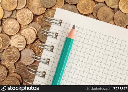 Notepad and pencil on a pile of coins