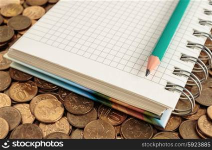 Notepad and pencil on a pile of coins