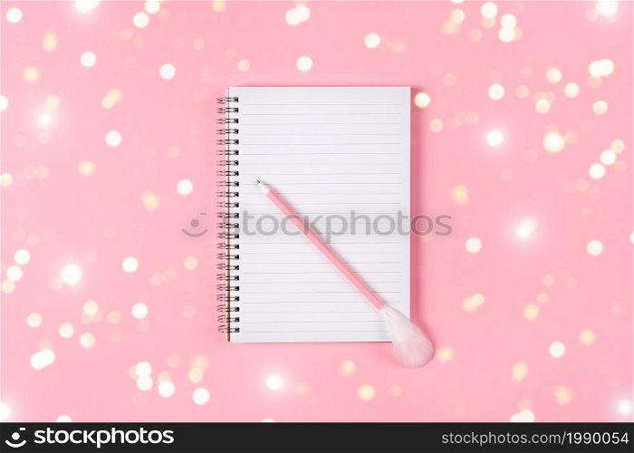 Notepad and pink pen decorated with feather on pink background. Holiday wish list concept.. Notepad and pink pen decorated with feather on pink background. Holiday wish list concept