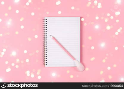 Notepad and pink pen decorated with feather on pink background. Holiday wish list concept.. Notepad and pink pen decorated with feather on pink background. Holiday wish list concept