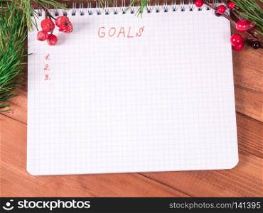 Notepad for writing resolution and goals for the New Year, spruce branches on a wooden background with copy space. goals for new year in blank open notebook