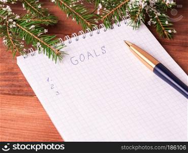 Notepad for writing resolution and goals for the New Year, spruce branches on a wooden background with copy space. Planning of the new year top view wooden background