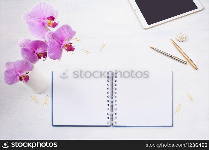 Notepad mockup with tablet, pen, golden paperclip and pink orchid on the white table