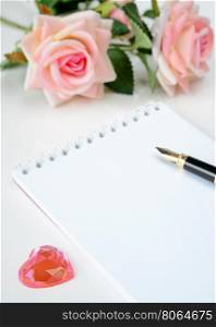 notepad with a pen, two roses and a glass heart