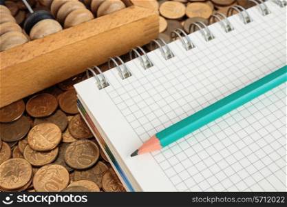 Notepad with pencil and abacus on a pile of coins