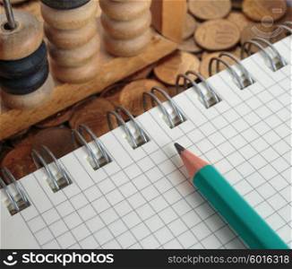 Notepad with pencil and abacus on a pile of coins