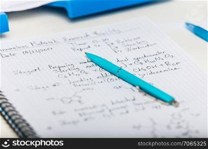 Notepad with scientific research report and blue pen on laboratory table with selective focus effect