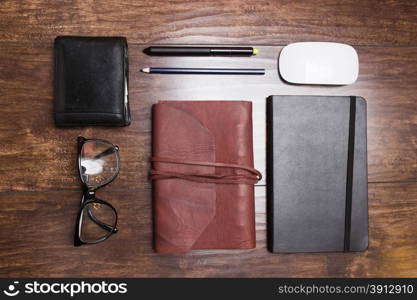 Notepads in leather cover with pencils and eyeglasses on wooden background