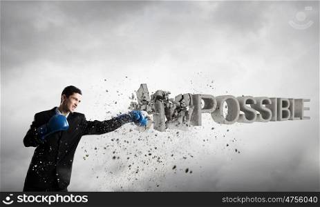 Nothing is impossible for him. Young businessman in blue boxing gloves breaking impossible word