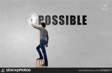 Nothing is impossible. Man changing word impossible in to possible by erasing part of word with paint brush
