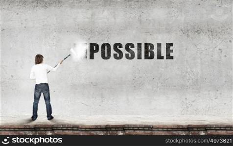 Nothing is impossible. Man changing word impossible in to possible by erasing part of word with paint roller