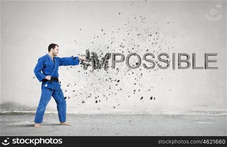 Nothing is impossible. Young determined karate man breaking stone impossible word