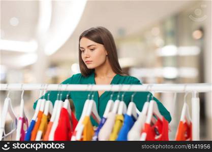 nothing to wear, clothing, sale, fashion and style concept - woman choosing clothes at shopping center or mall