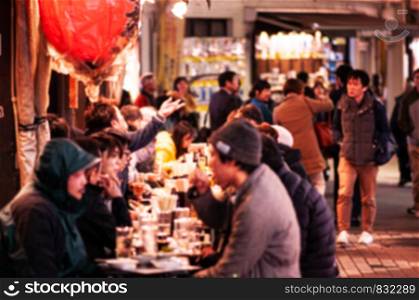 NOV 29, 2018 Tokyo, Japan - Ameyoko market vibrant busy food street night life in Ueno district with blurry out focus tourists eating and drinking at street side Izakaya restaurant