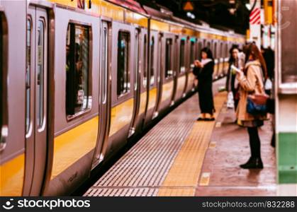 NOV 29, 2018 Tokyo, Japan - Tokyo JR train Chuo Sobu line stop at station platform with blurry out focus female passengers in winter clothes using smart phone
