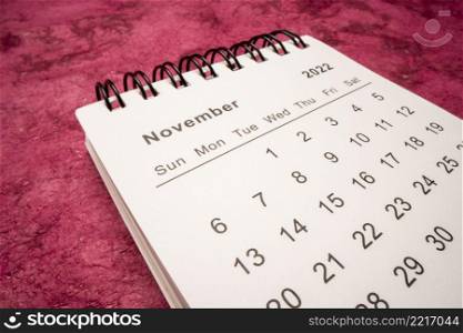 November 2022 - spiral desktop calendar against textured handmade paper, low angle macro shot, time and business concept
