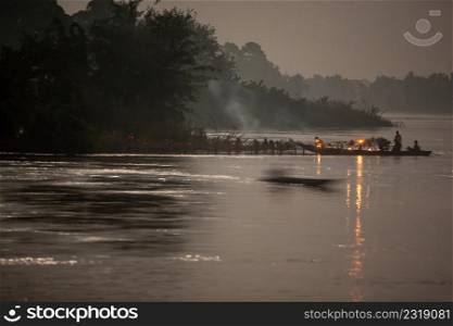 Novice monks and boy lighting a candle on wooden boat in the festival of the illuminated boat procession. Mekong River, Don Det Island, Si Phan Don, Champasak, South Laos. Noise, Grain. Long exposure.