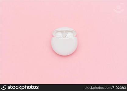 Novosibirsk, Russia - March 22, 2019: White wireless Bluetooth headphones and charging case on pink paper background. Template for text or your design. Flat lay Top view Copy space.. Novosibirsk, Russia - March 22, 2019: White wireless Bluetooth headphones in charging case on pink paper background. Template for text or your design. Flat lay Top view Copy space