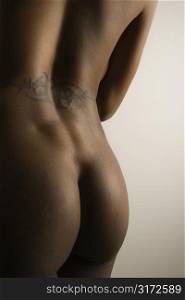Nude African American mid adult female buttocks and back with tattoo.