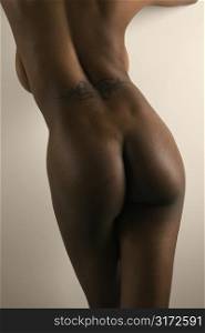 Nude African American mid adult female standing with back tattoo.