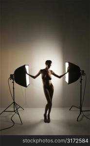 Nude African American mid adult woman standing between soft boxes in photography studio.